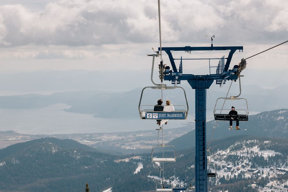 Ski lift chairs ascending a snowy mountain with distant lake views.
