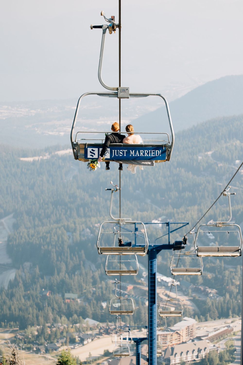 Just married couple riding on a ski lift with mountain views in the background.