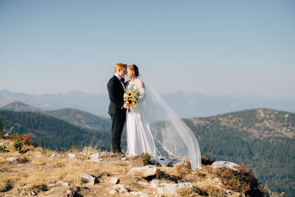 Wedding couple embracing on mountain peak with dramatic mountain vista behind them.