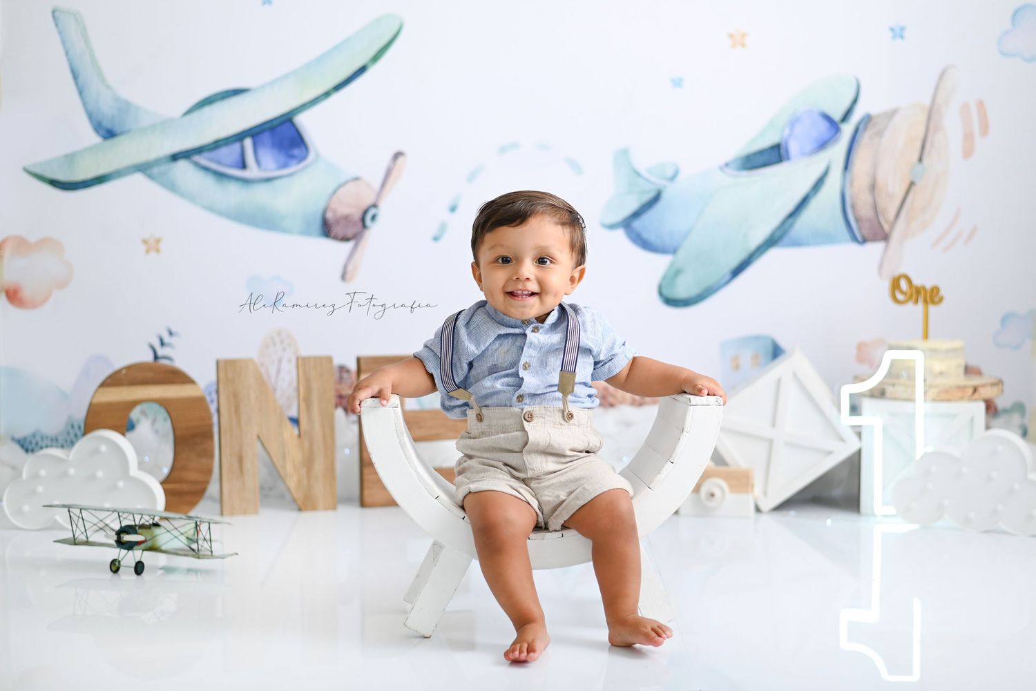 Baby in white shorts stands in front of aviation-themed wall decor with blue toy airplanes and clouds.