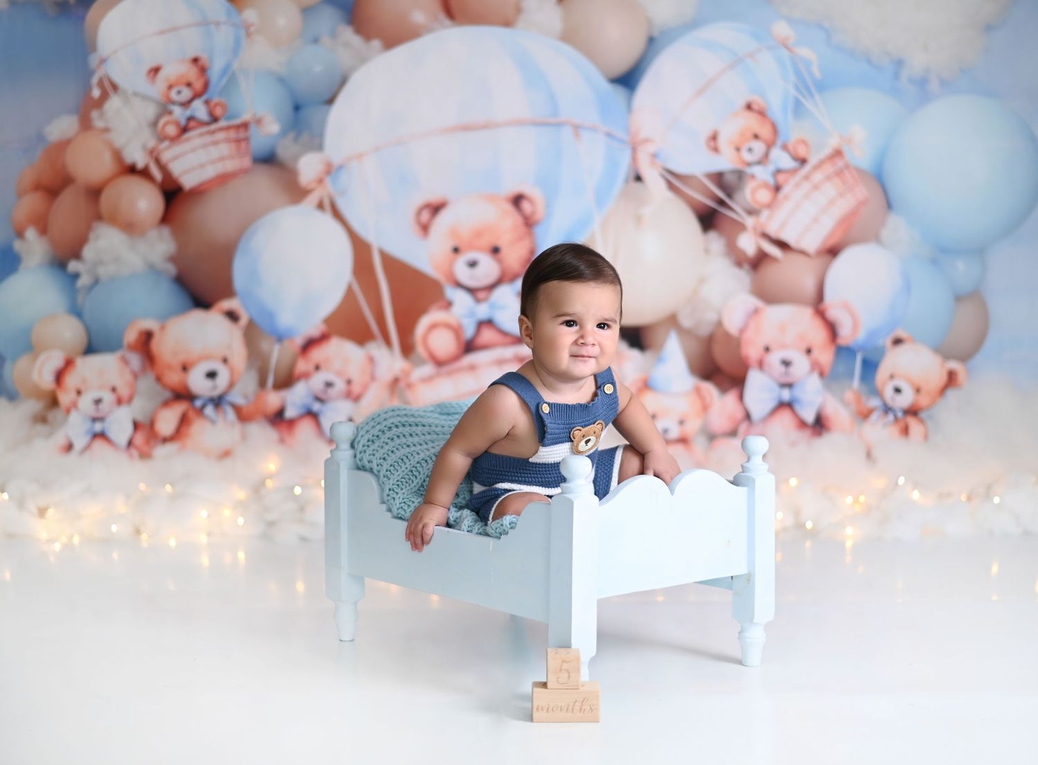 A baby photoshoot setup with soft pink and blue balloons, plush toys, and twinkling lights creating a dreamy atmosphere.