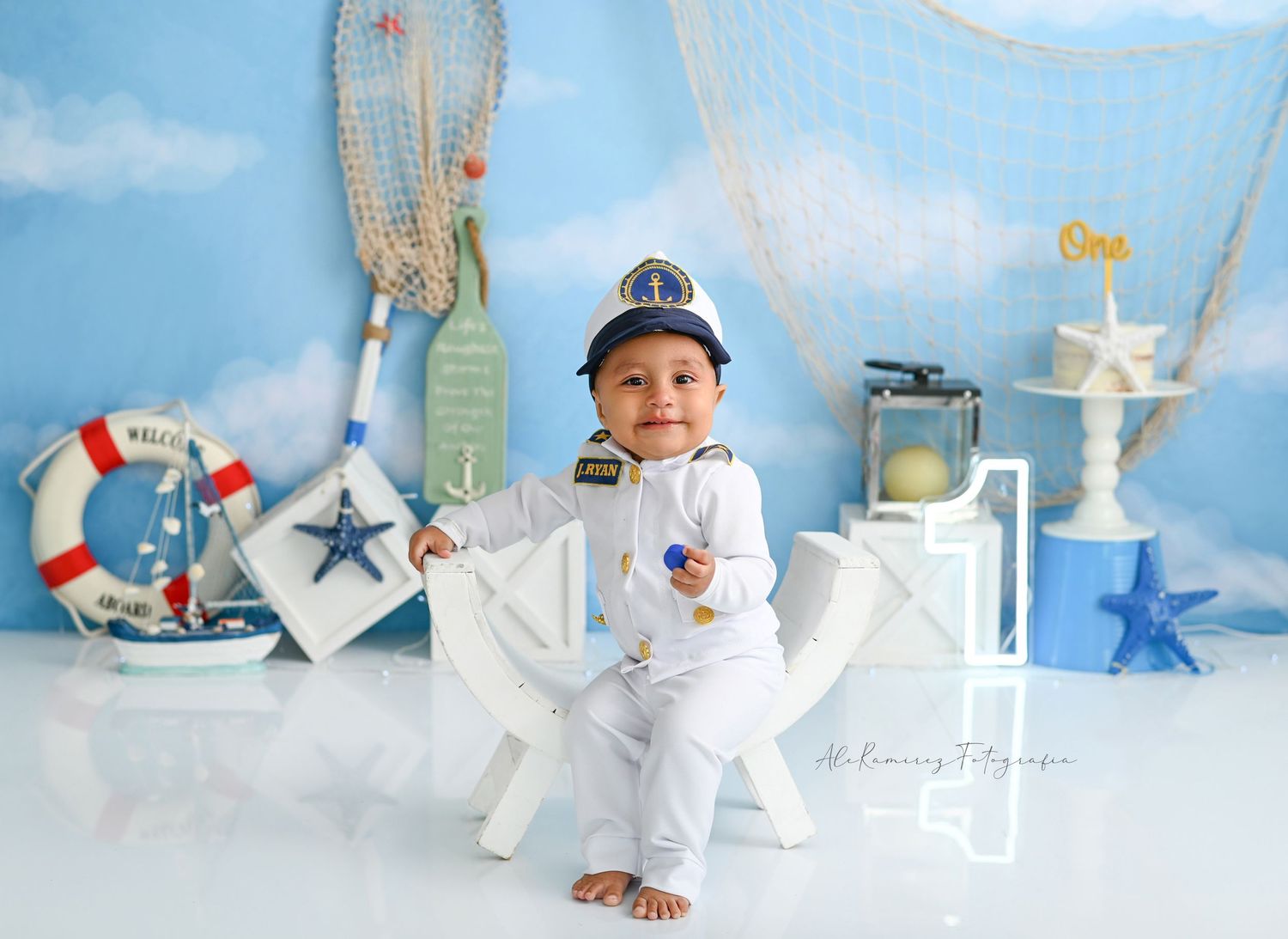 Nautical themed baby photo setup with white wood props, fishing net decor, and blue sky background staging.