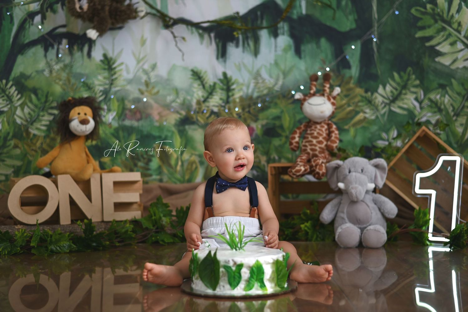 Safari themed first birthday cake smash scene with jungle decorations, stuffed animals and 'ONE' lettering display.