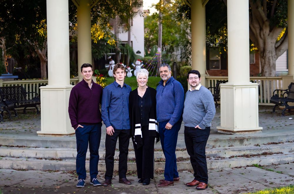 A group of people stand together in formal attire against a backdrop of white columns and trees.