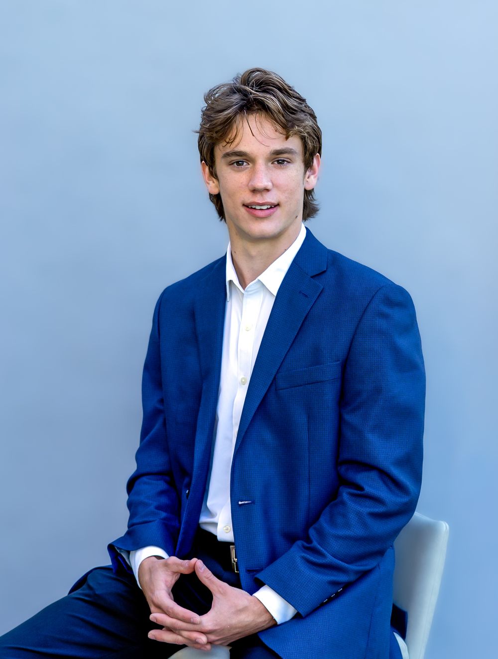 Professional studio portrait series showing someone in a navy blue blazer and white dress shirt against a light blue background.