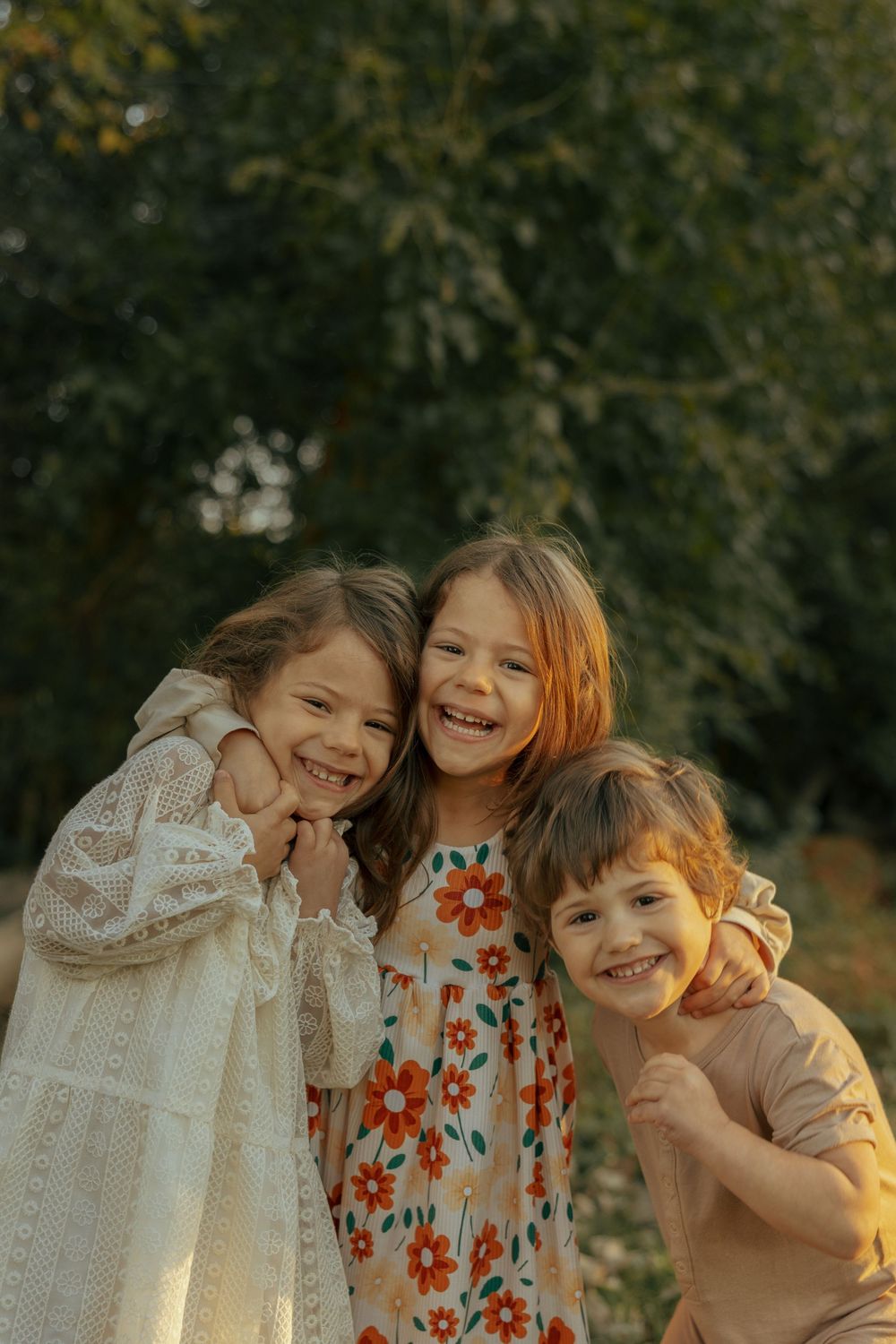 Three children share joyful laughter while embracing outdoors in warm sunlight.