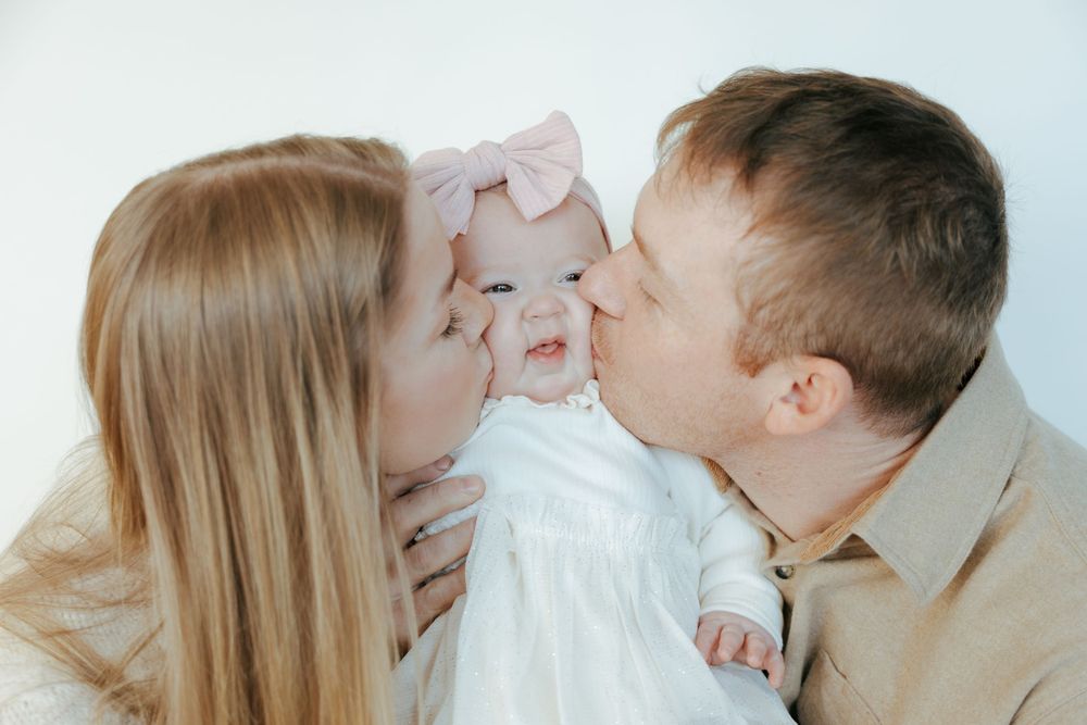 A loving family in white outfits shares tender moments together during a photo session against a light background.