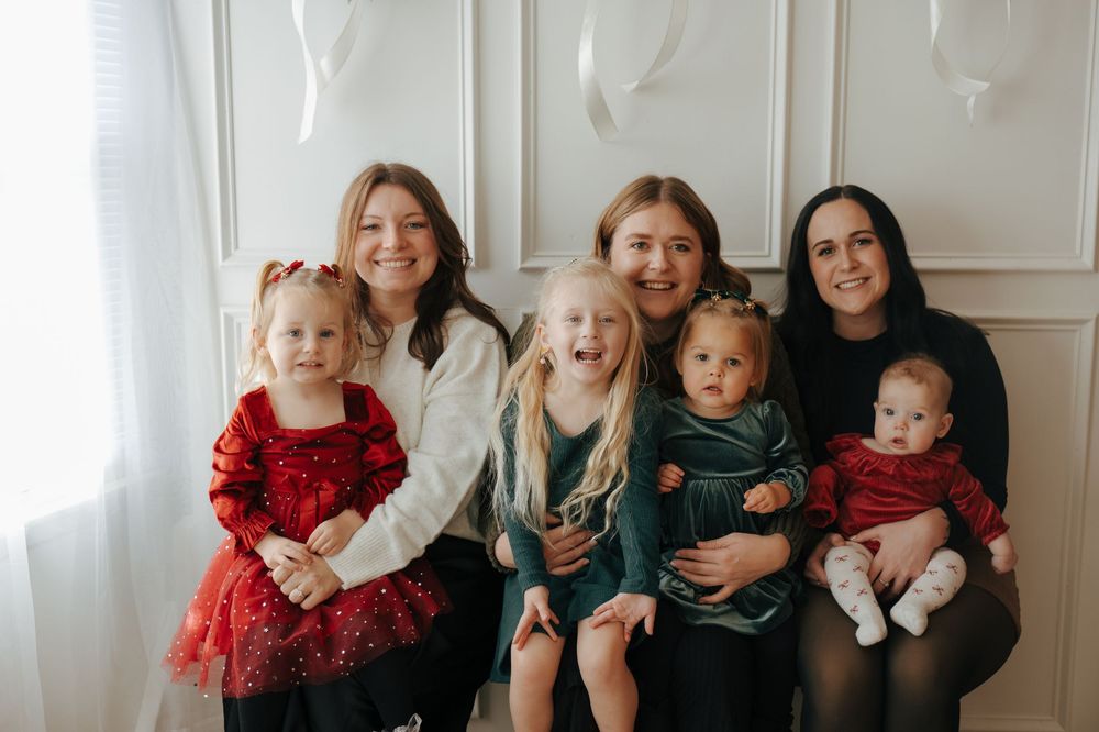 A group of people in coordinating outfits pose together for a holiday family photo against a white wall.