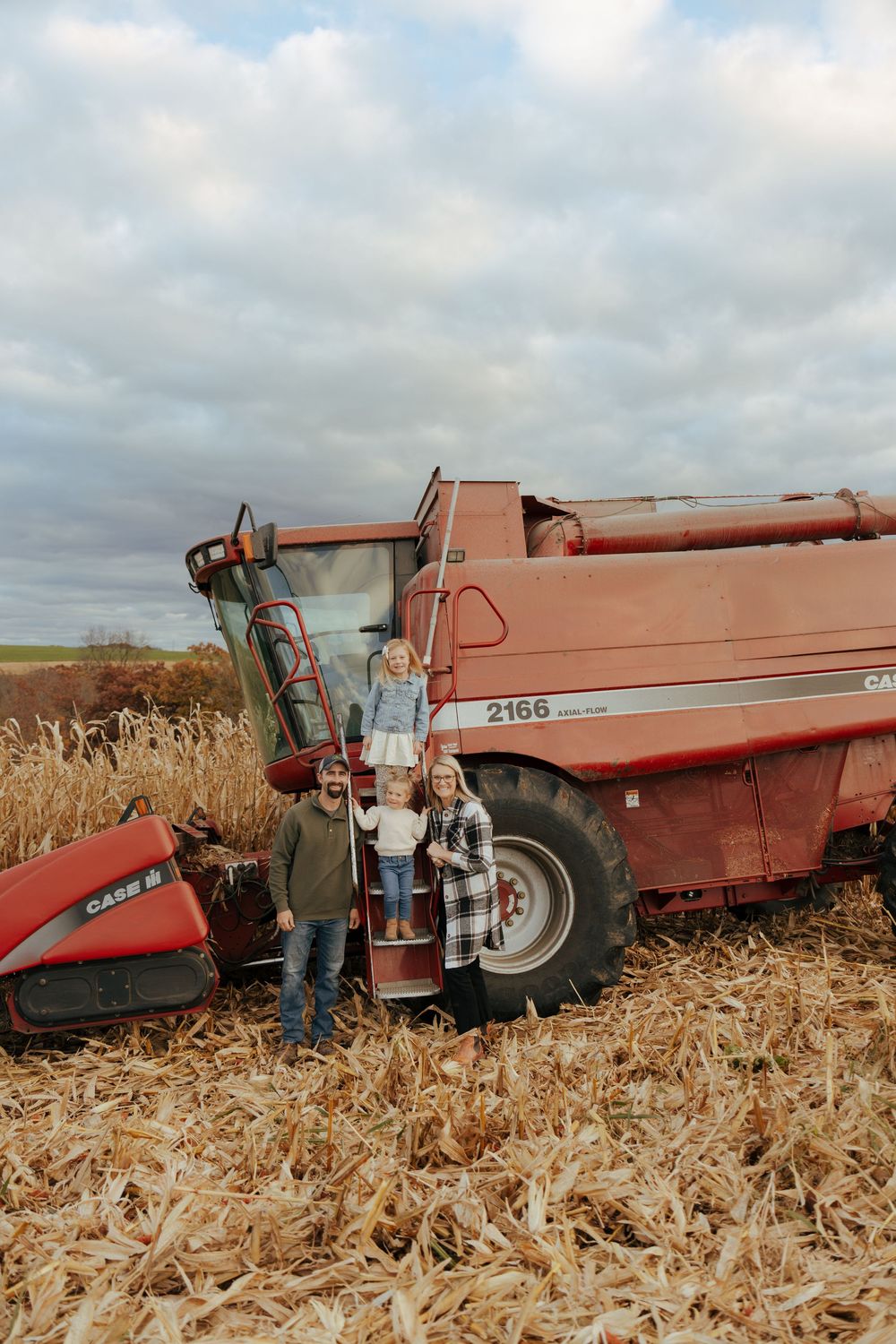 A large red Case IH combine harvester stands in a harvested corn field on a cloudy autumn day.