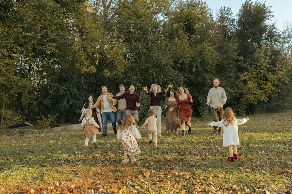 Group of people running and playing together in a field covered with yellow autumn leaves on a sunny day.
