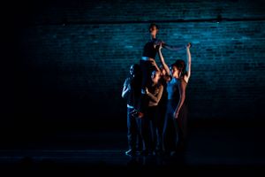 Contemporary dancers perform an intimate piece in dramatic blue lighting on a dark stage.