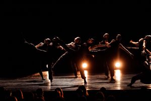 Silhouetted dancers perform in dramatic spotlights on a dark stage.