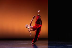 A contemporary dance performance featuring a dramatic lift against an orange-lit backdrop.