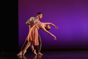 Two dancers perform an intimate contemporary duet against a purple-lit stage.