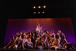 A large ensemble creates a dramatic group formation under purple stage lighting.