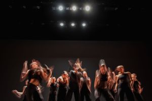 Dancers raise their arms in an expressive group performance under stage lighting.