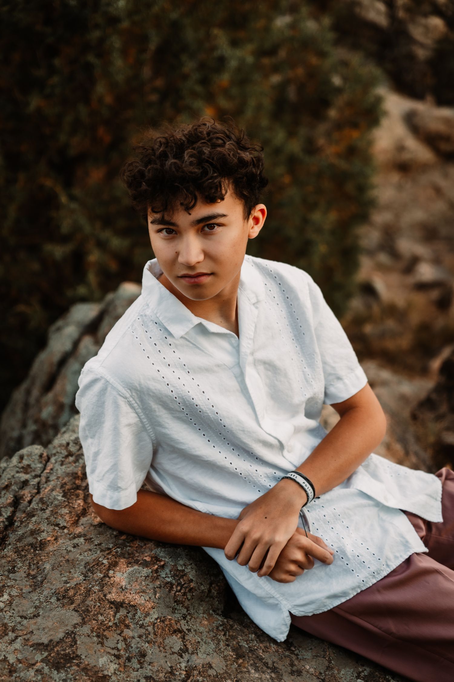 Portrait of someone in a white eyelet shirt sitting on rocks in warm natural lighting.