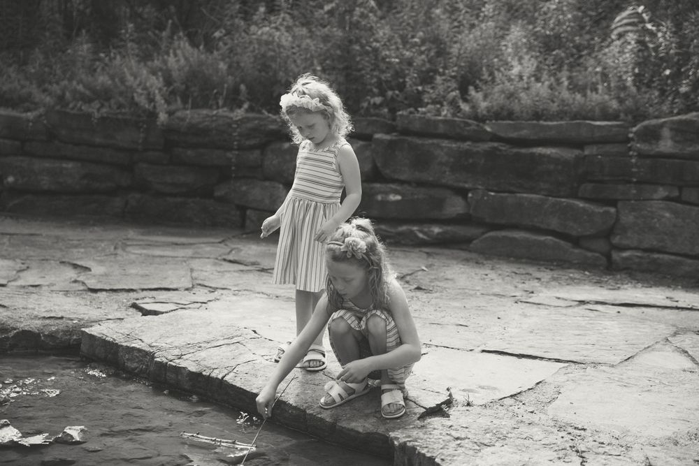 A small child in a dress plays on an outdoor stone patio in a black and white vintage photograph.