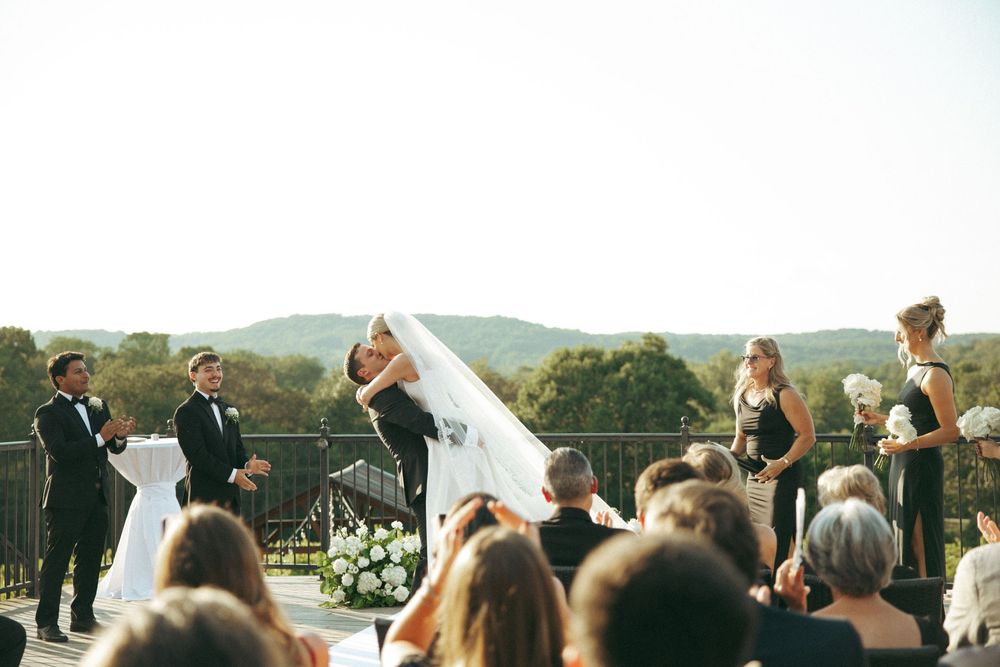 A beautiful outdoor wedding ceremony on a terrace overlooking scenic mountains with guests seated in rows.