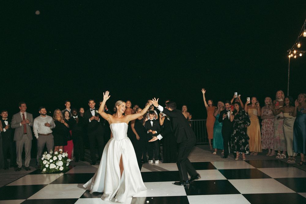 Happy couple celebrates with guests on a dark dance floor during their wedding reception first dance.