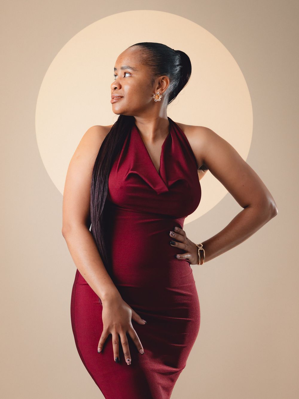 A person in a burgundy dress poses against a beige backdrop in a series of elegant maternity portraits.