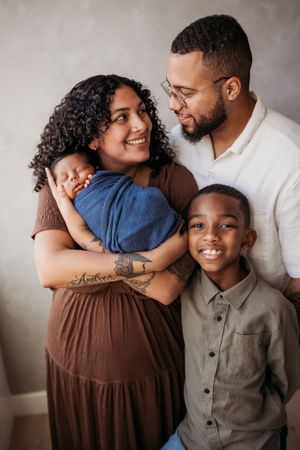family with mother and father smiling at each other. Newborn is sleeping and brother is smiling at the camera.