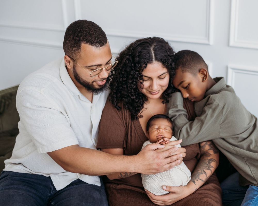 Family embracing on couch. Newborn in ivory swaddle.