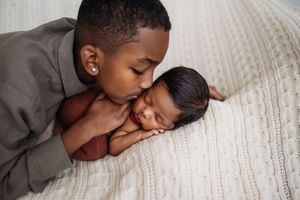 brother kissing newborn baby asleep