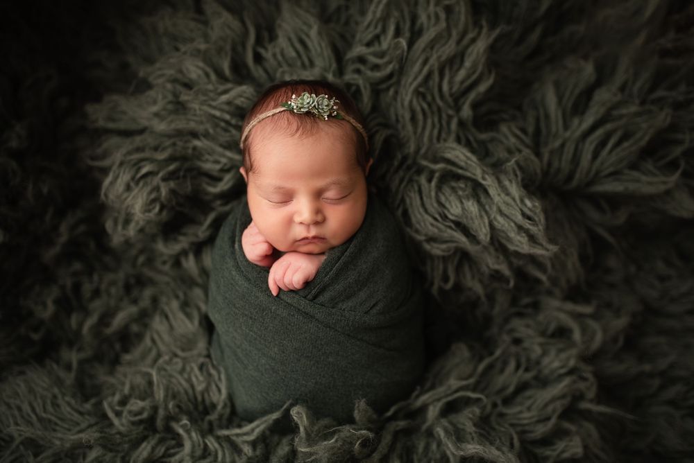 newborn wrapped in green swaddle on a green flokati rug.