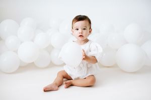 first birthday photoshoot in Nottinghamshire with baby wearing white romper, surrounded by white balloons holding a balloon