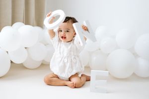 first birthday photoshoot in Nottinghamshire with little girl in white romper, with white balloons and holding white one letters