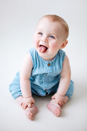 Photos showing a baby in blue outfit sitting on a white background, expressing joyful smiles and movements.