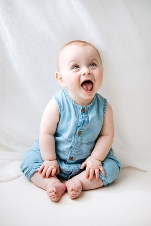 A baby in light blue shirt and shorts sits on white backdrop showing various playful expressions and poses.