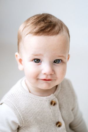 Sweet baby wearing a cream colored knit sweater with wooden buttons smiles at camera in studio portraits.
