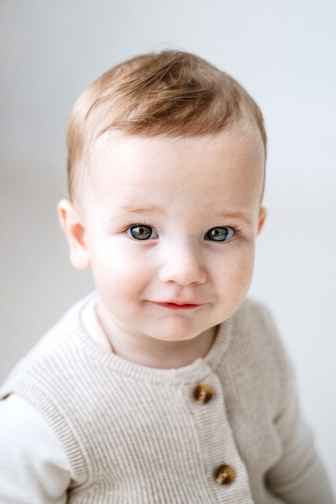 Sweet baby wearing a cream colored knit sweater with wooden buttons smiles at camera in studio portraits.