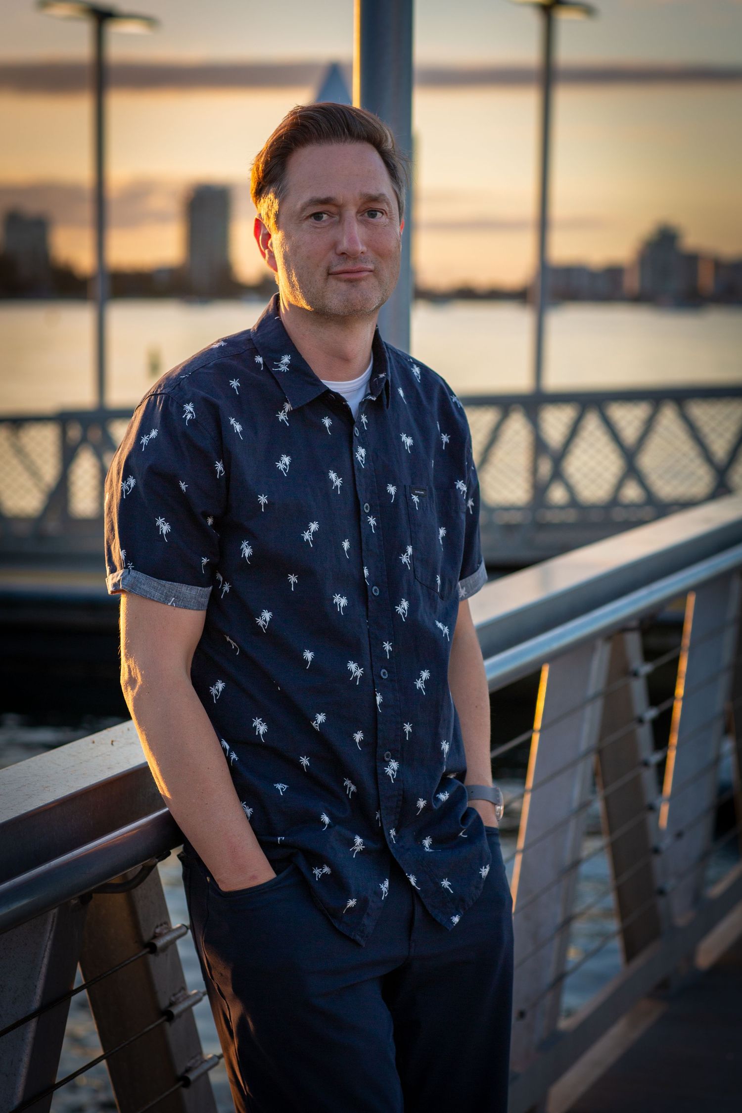 A casual portrait of a person in a patterned shirt at sunset on a waterfront deck.