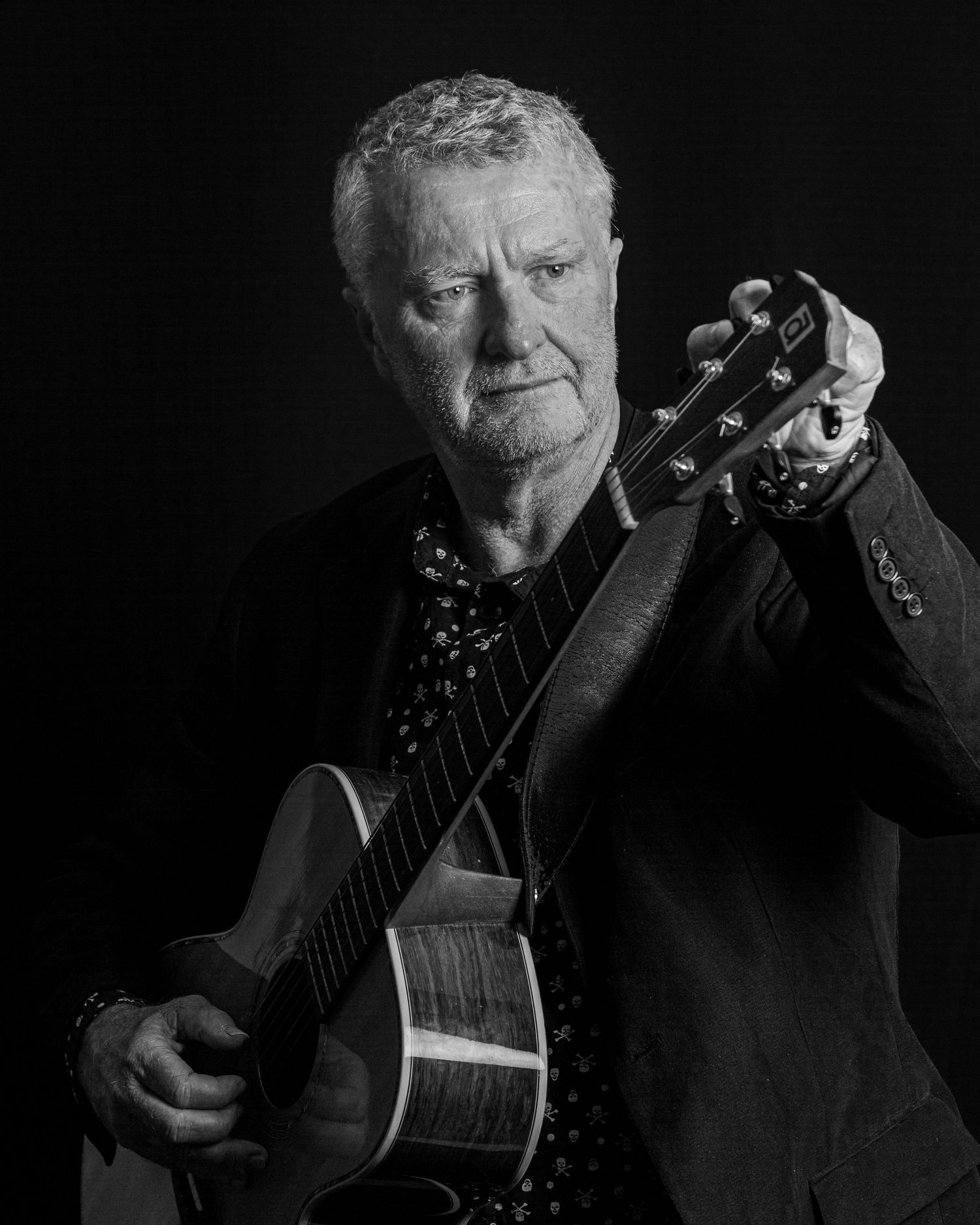 Black and white portrait of musician holding acoustic guitar against dark background.