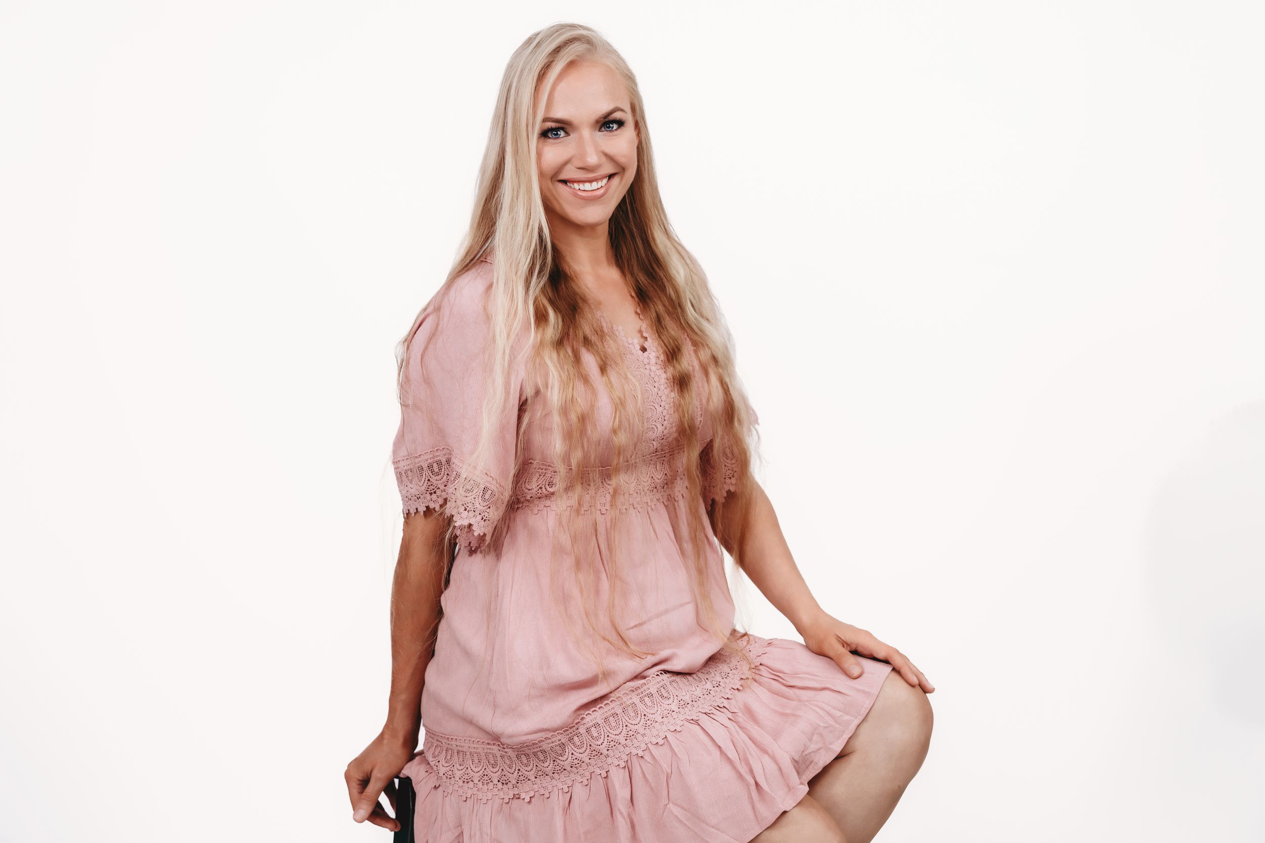 A person wearing a pink ruffled dress poses against a white background in a studio setting.