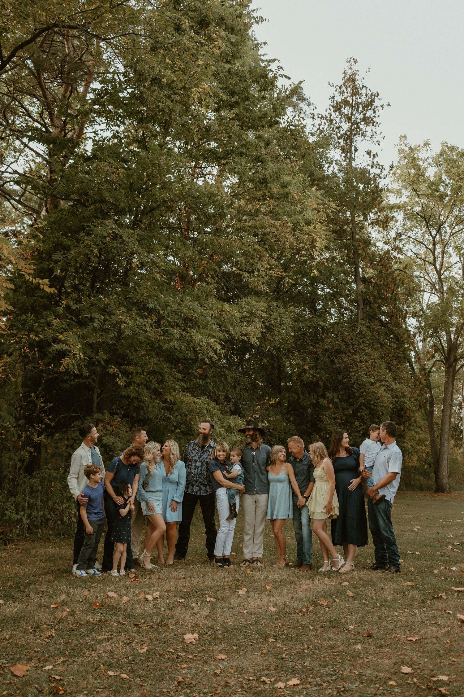A large group poses together in a pine forest with tall trees creating a dramatic backdrop.