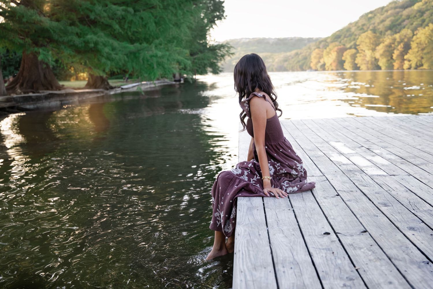 A couple sits together on a wooden dock overlooking a serene lake surrounded by autumn trees.