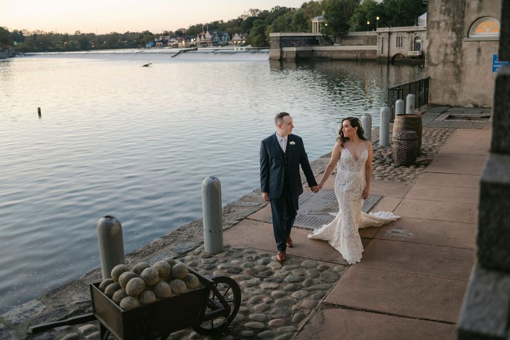 A couple walks hand in hand along a waterfront promenade at sunset at Philadelphia's Water Works wedding venue