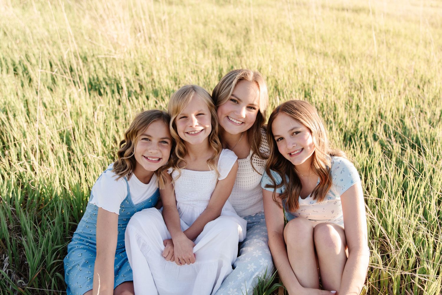 Four people sitting close together in a grassy field during golden hour.