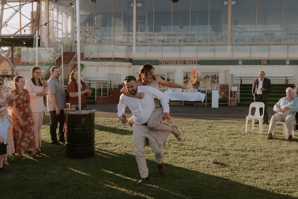A group of people dance together on a grassy lawn at an outdoor wedding reception during golden hour.