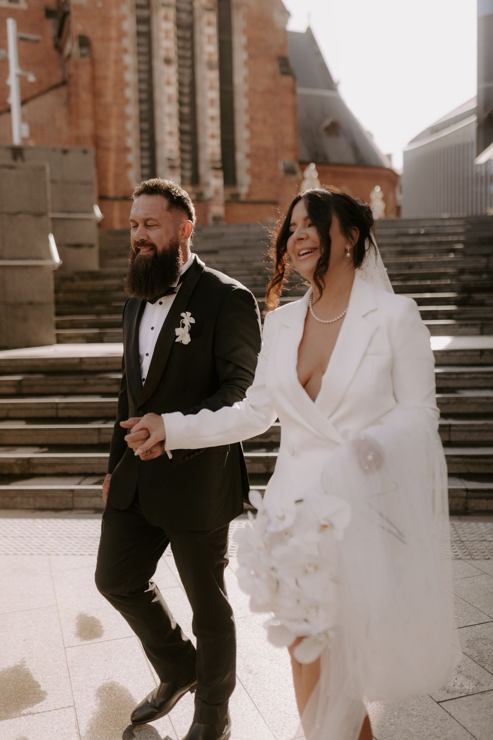 Candid moments of a couple laughing and dancing on stone steps outside a church.