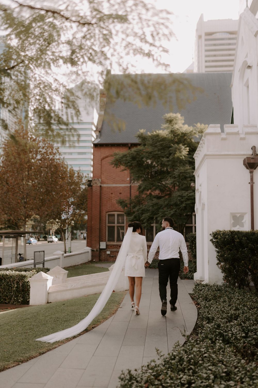 A romantic first look sequence between a couple walking together on a church pathway surrounded by greenery.