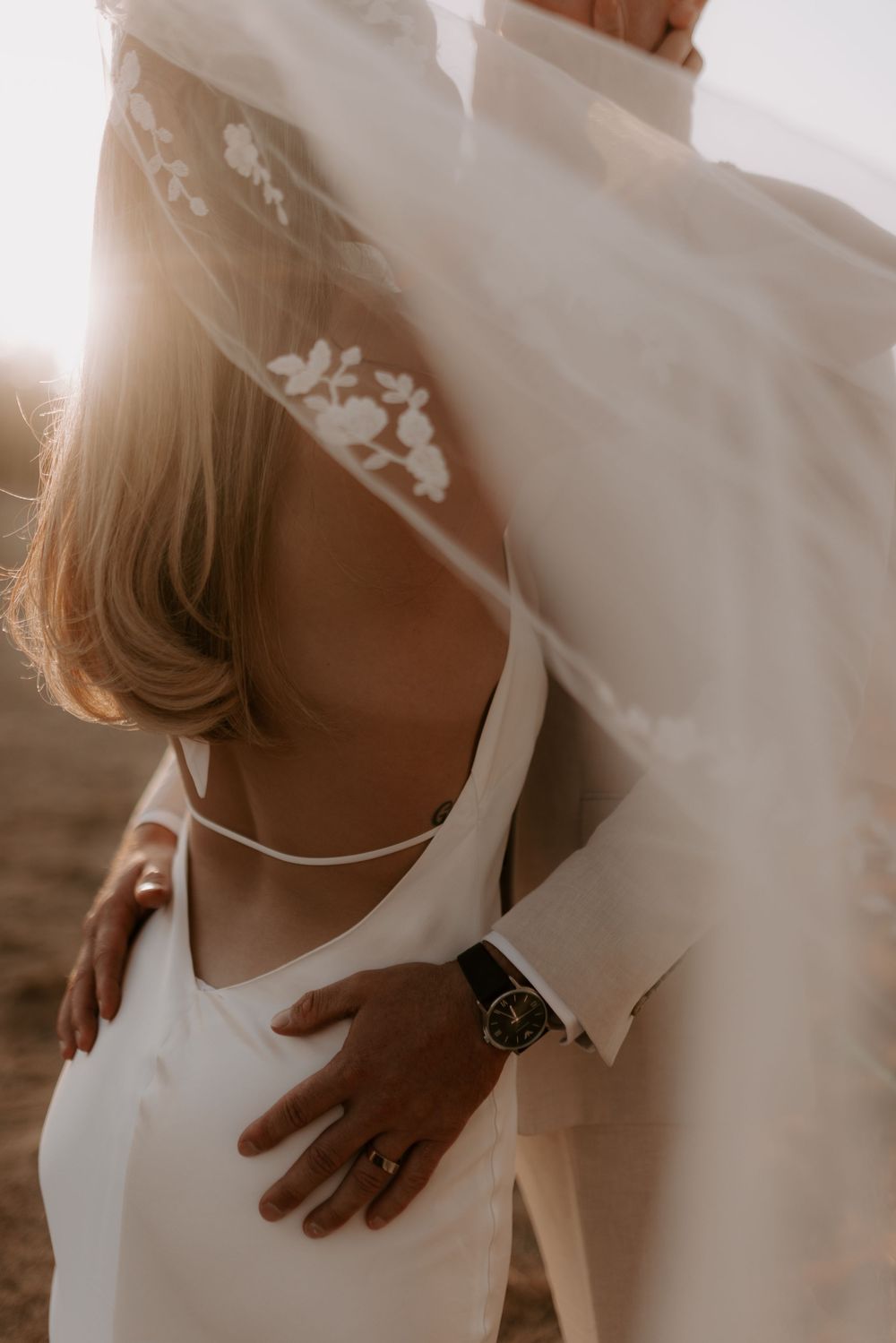 Close-up detail of a bride in a white wedding dress with delicate lace details and a watch accessory.