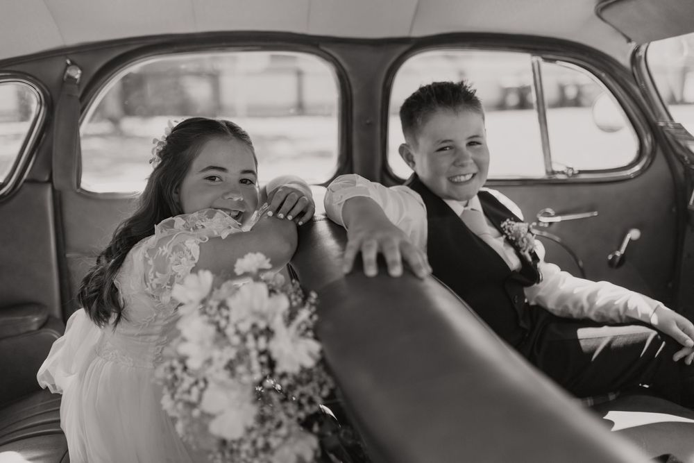 Newlywed couple shares a joyful moment in the back seat of a vintage car during their wedding celebration.