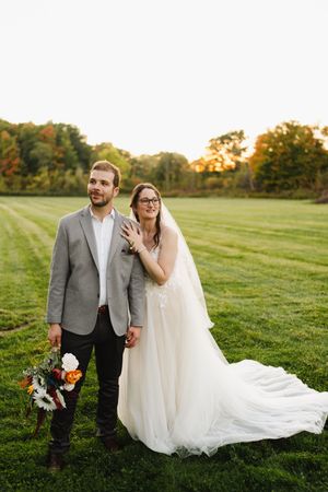 A couple in wedding attire shares a romantic moment together on a grassy field during golden hour.