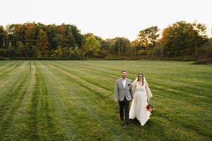 A couple stands together on a freshly mowed green lawn with autumn trees in the background at sunset.