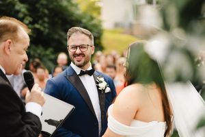 Elegant outdoor wedding ceremony with guests seated in white chairs under trees during a beautiful autumn day.